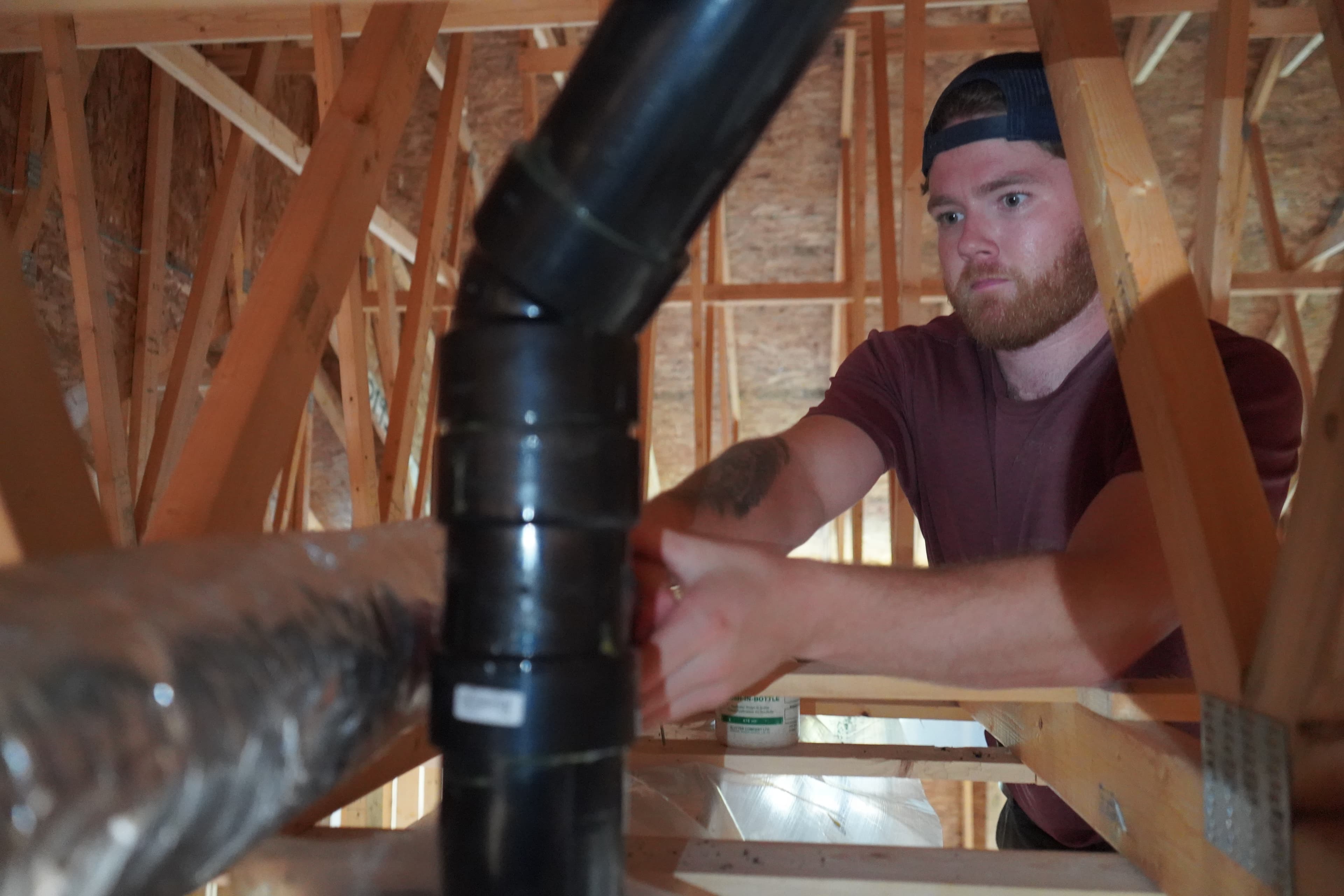A tradesperson fitting plumbing pipe inside wood framing