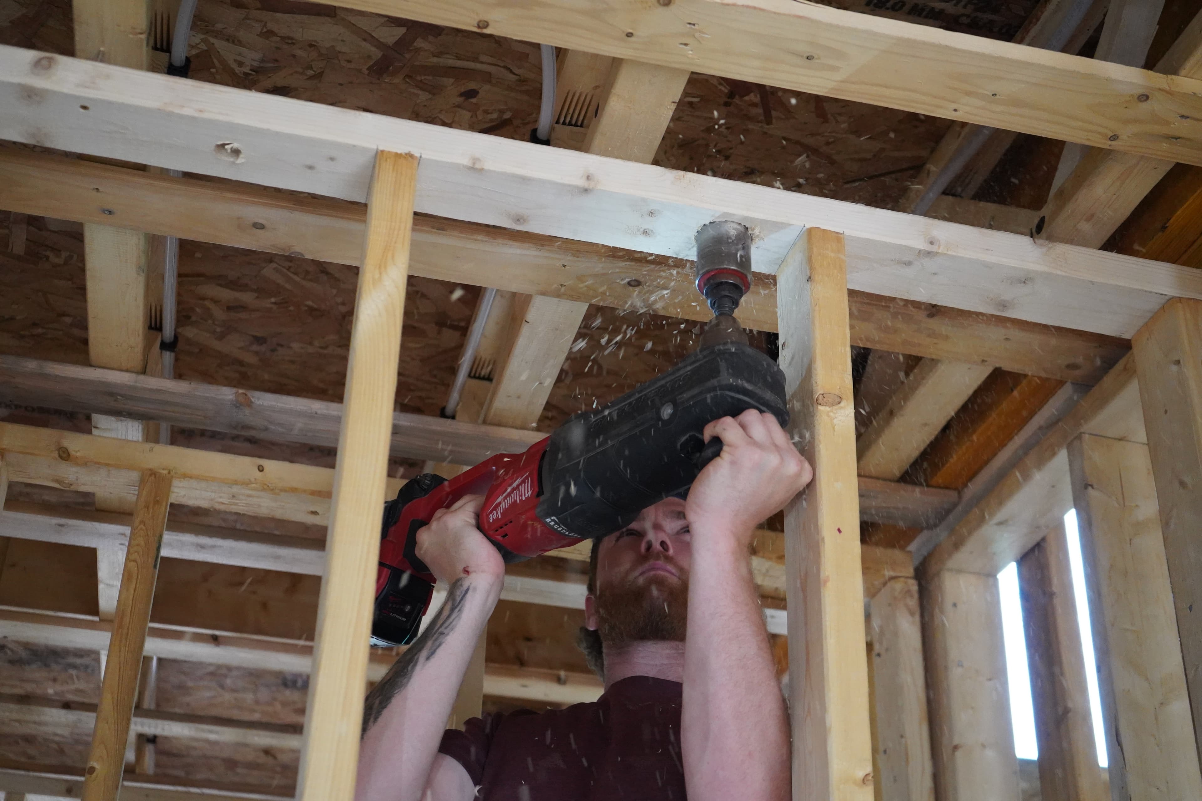 A tradesperson drilling a hole through wood framing with a hole saw