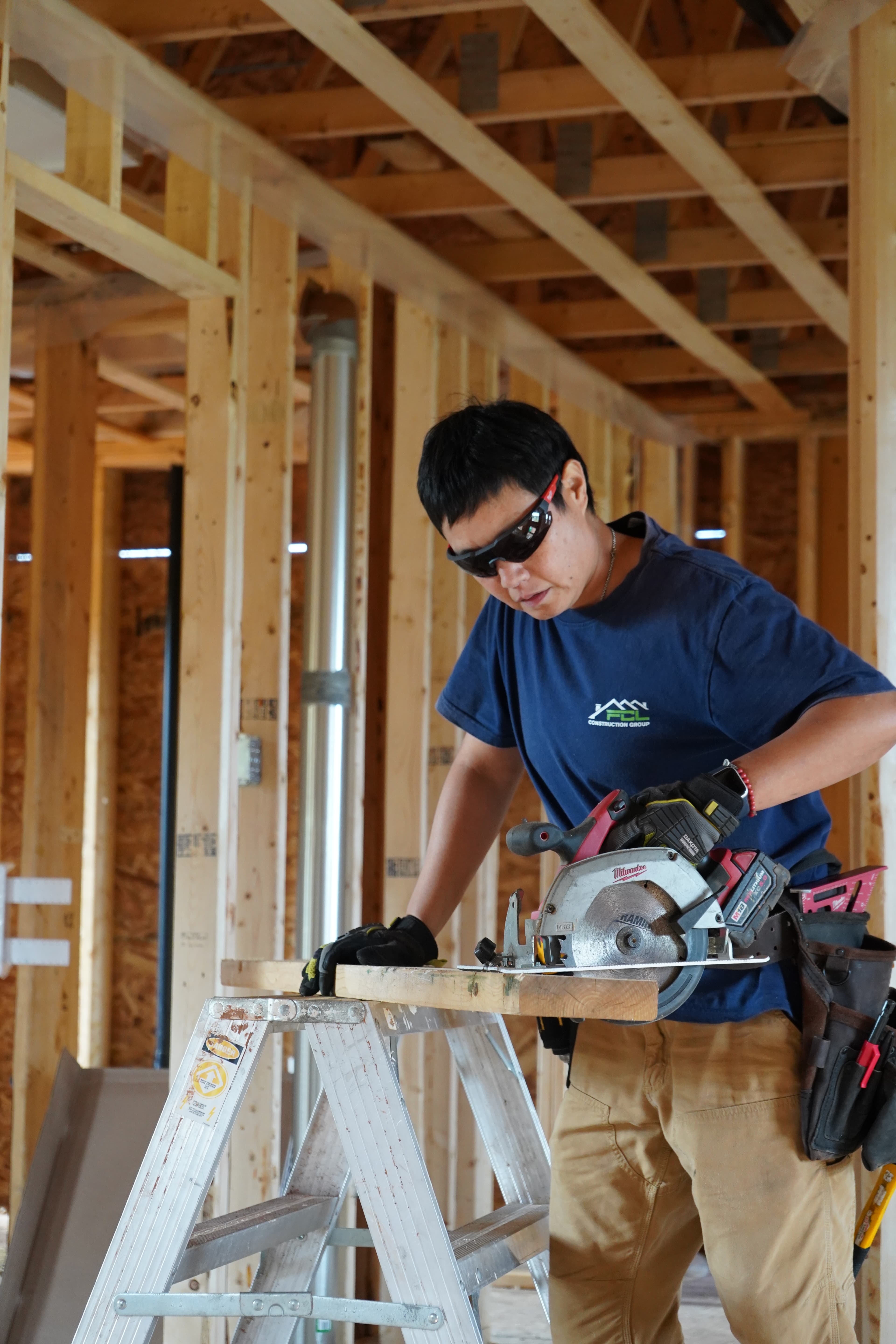 A tradesperson cutting lumber on a sawhorse inside a framed house