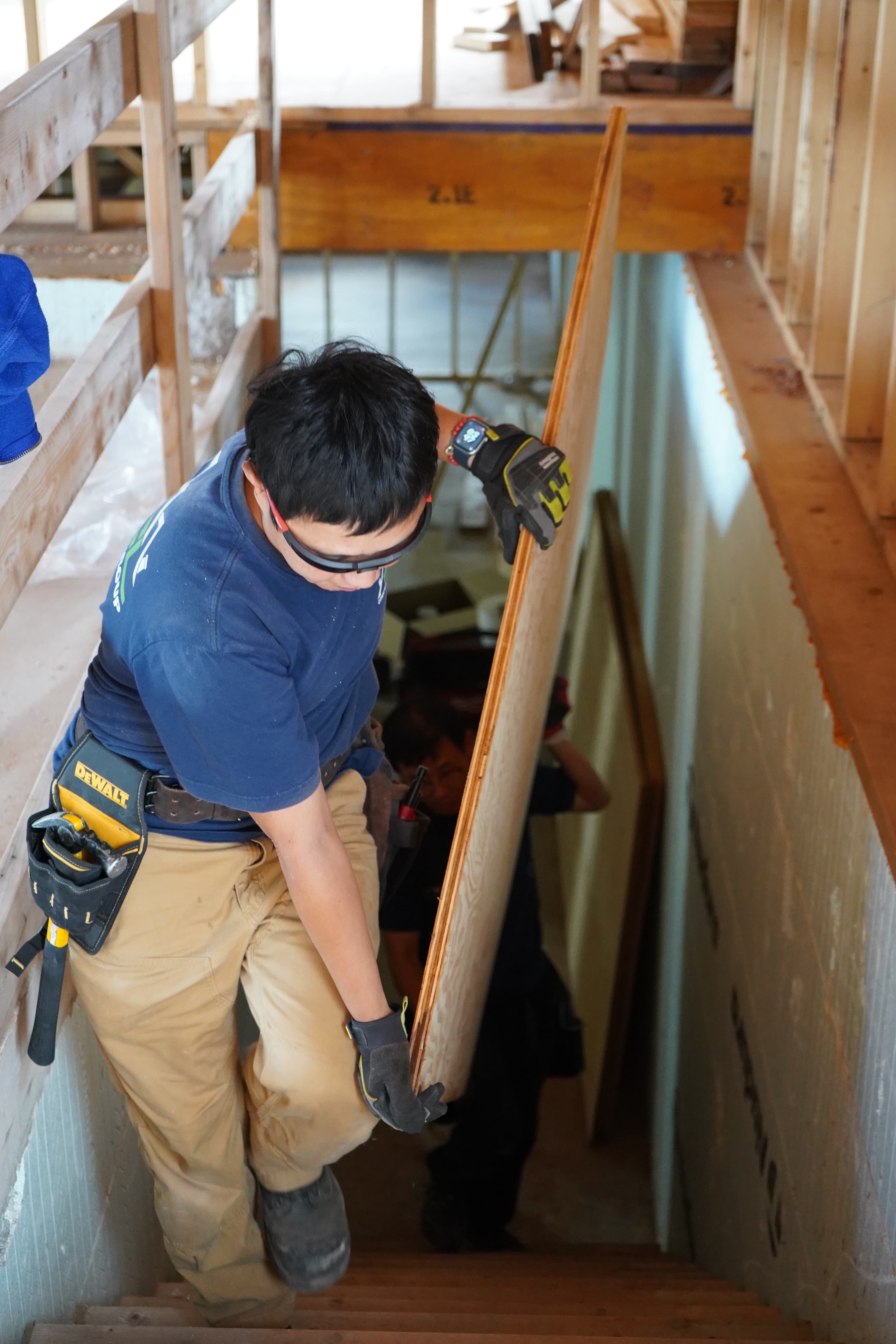 A tradesperson carrying a plywood sheet down a jobsite stair