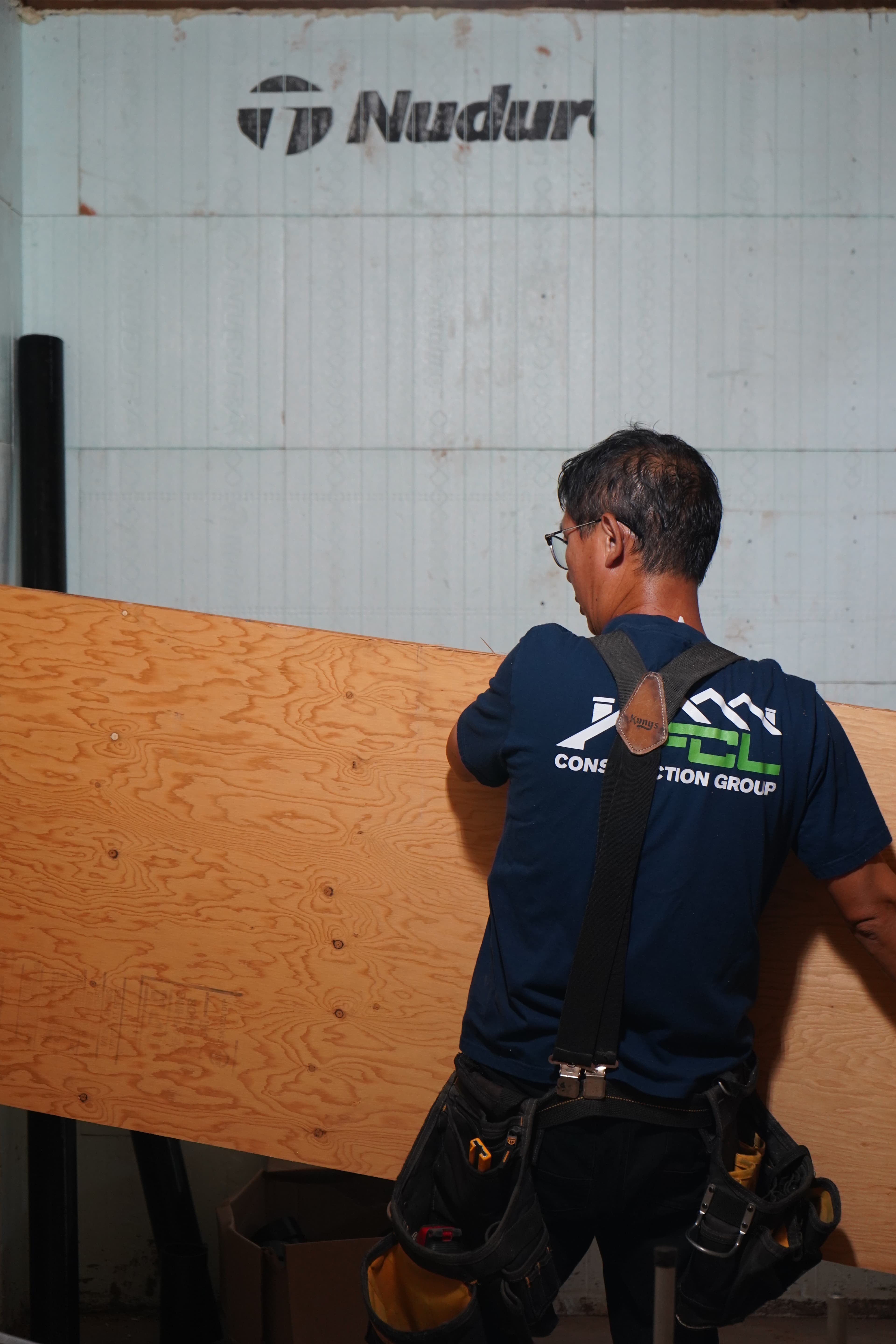 A tradesperson carrying a sheet of plywood across the jobsite